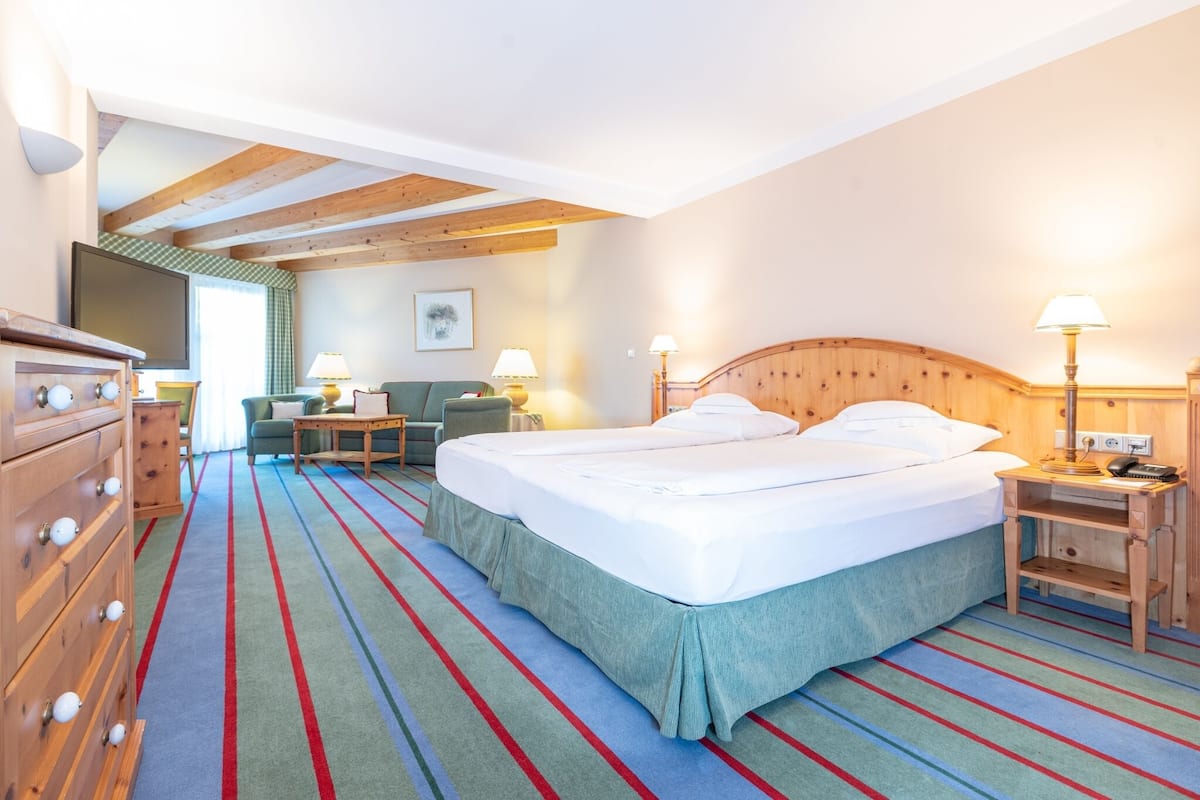 A hotel room with a bed, a dresser, a TV, a chair, and a desk with a lamp.