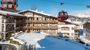 A hotel with a traditional Alpine architectural style, featuring a balcony with a snow-covered roof, a ski lift in operation, and a mountainous backdrop. - Hotel Kaiserhof Kitzbuehel (Kitzbuhel)