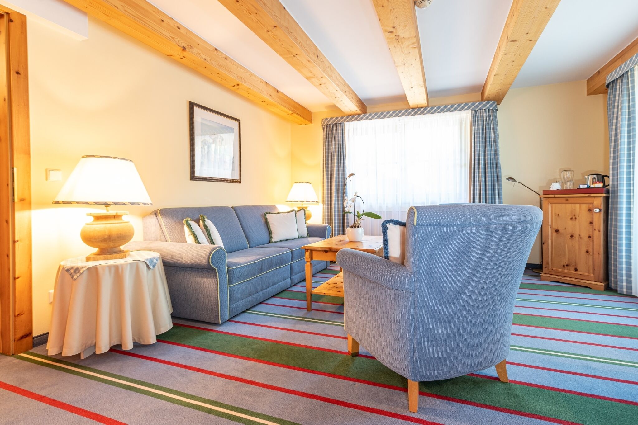 Una sala de estar acogedora con un sofá, un sillón y una mesita de centro. Hay un armario de madera y una ventana con cortinas.