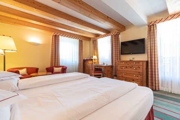 A hotel room with a large bed, a desk, a chair, a TV, and wooden beams on the ceiling.