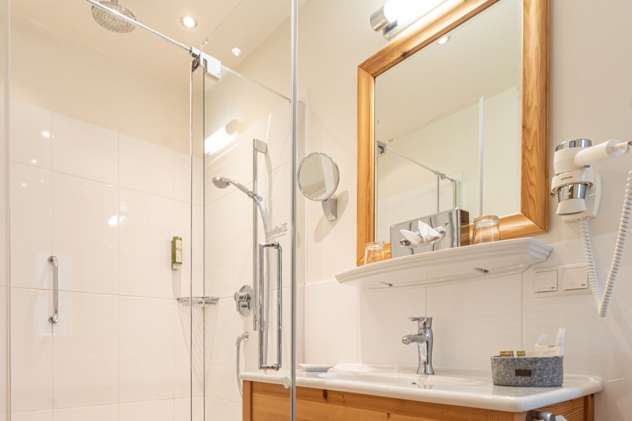 Un baño moderno con cabina de ducha de vidrio, tocador con lavabo, espejo y secador de pelo montado en la pared.