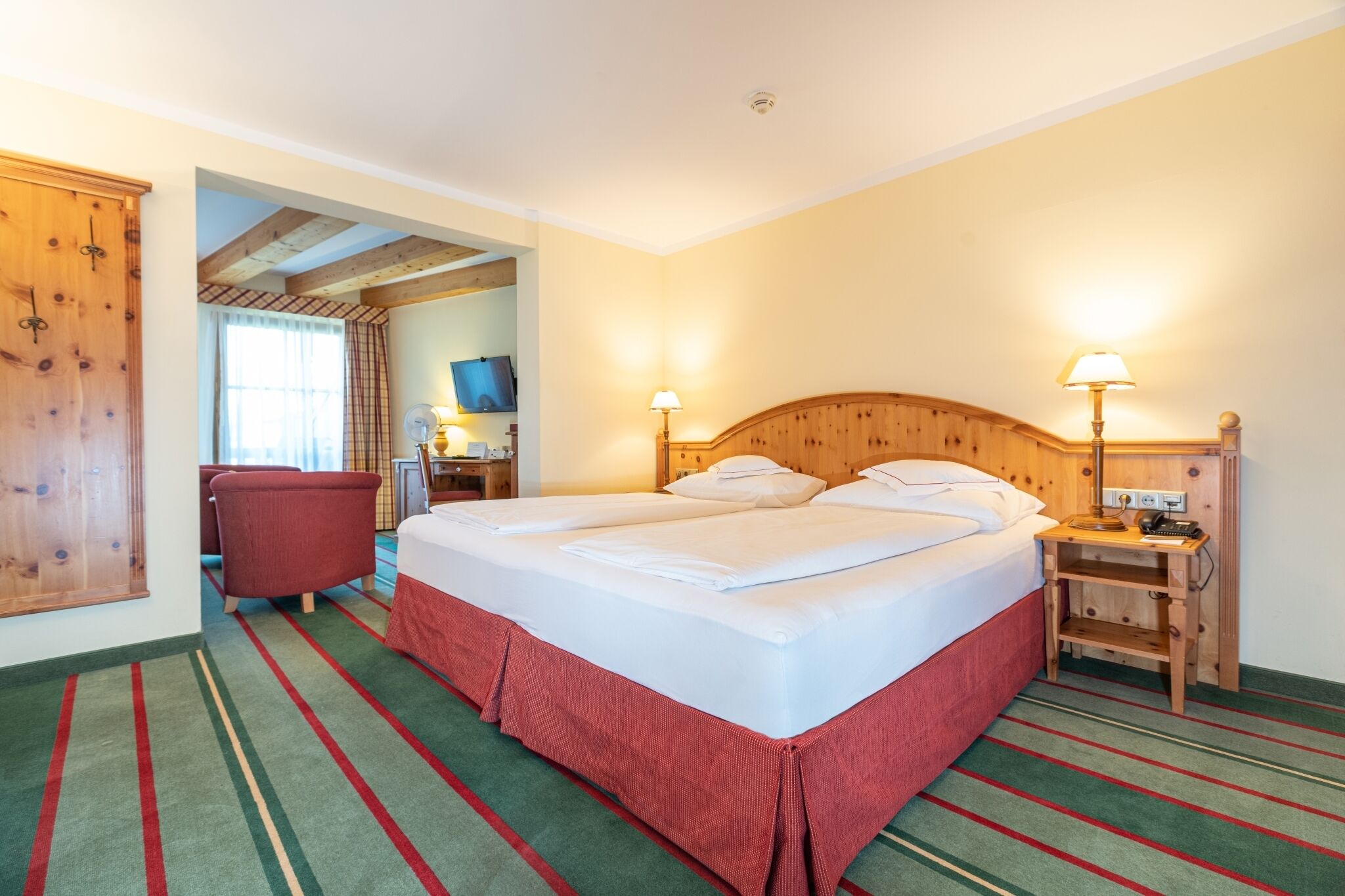 A double bed with a wooden headboard, a nightstand with a lamp, a red chair, and a wooden wardrobe.