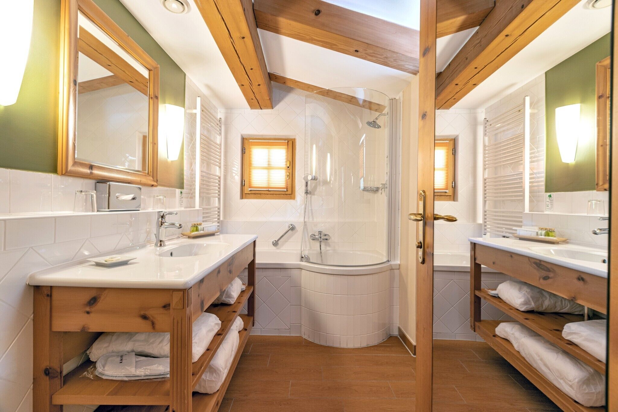 Ein Badezimmer mit zwei Waschbecken, einer Dusche, Holzregalen und einem großen Spiegel.