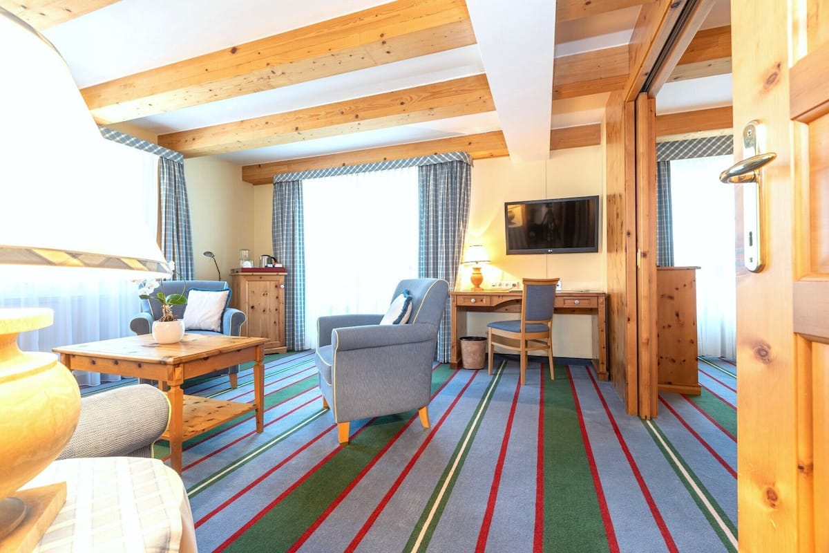A room with a wooden ceiling, a desk with a chair, a television, and a window with curtains.