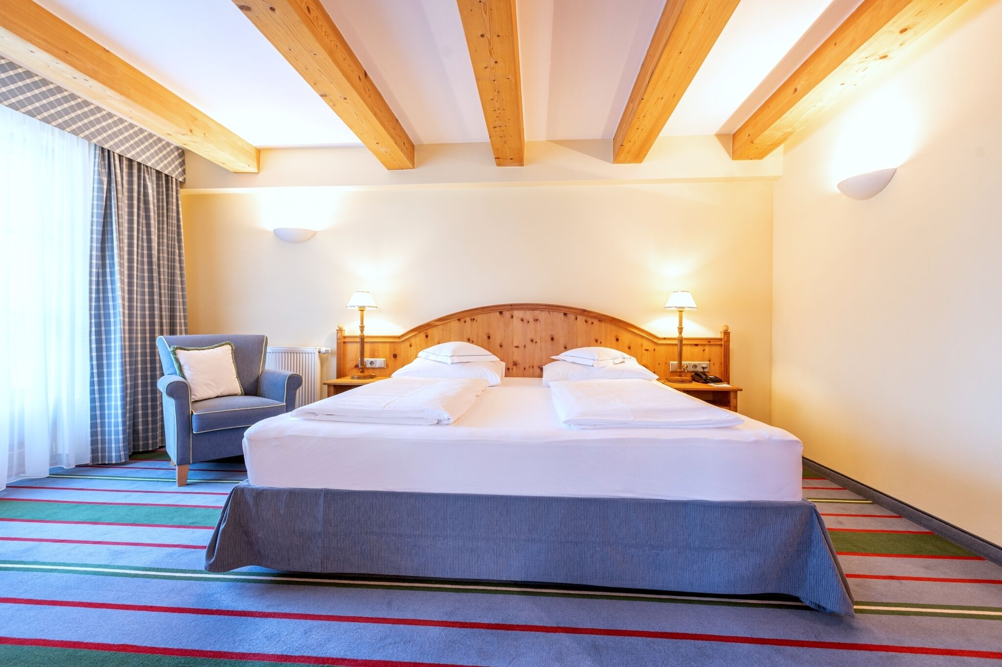 Una habitació d'hotel amb un llit gran, una cadira, una làmpada i una finestra amb cortines.