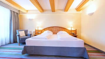 Una habitació d'hotel amb un llit gran, una cadira, una làmpada i una finestra amb cortines.
