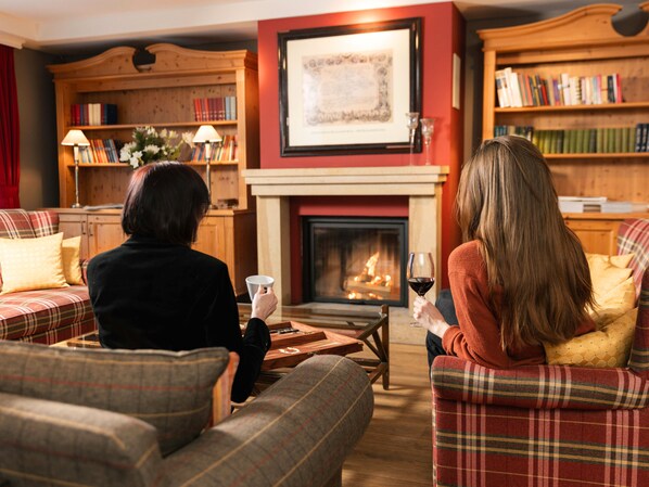A cozy living room with a fireplace, bookshelves, and plaid-patterned furniture. - Hotel Kaiserhof Kitzbuehel (Kitzbuhel)