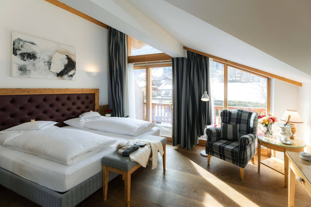 A bedroom with a large bed, a chair, a small table, and a window with curtains.