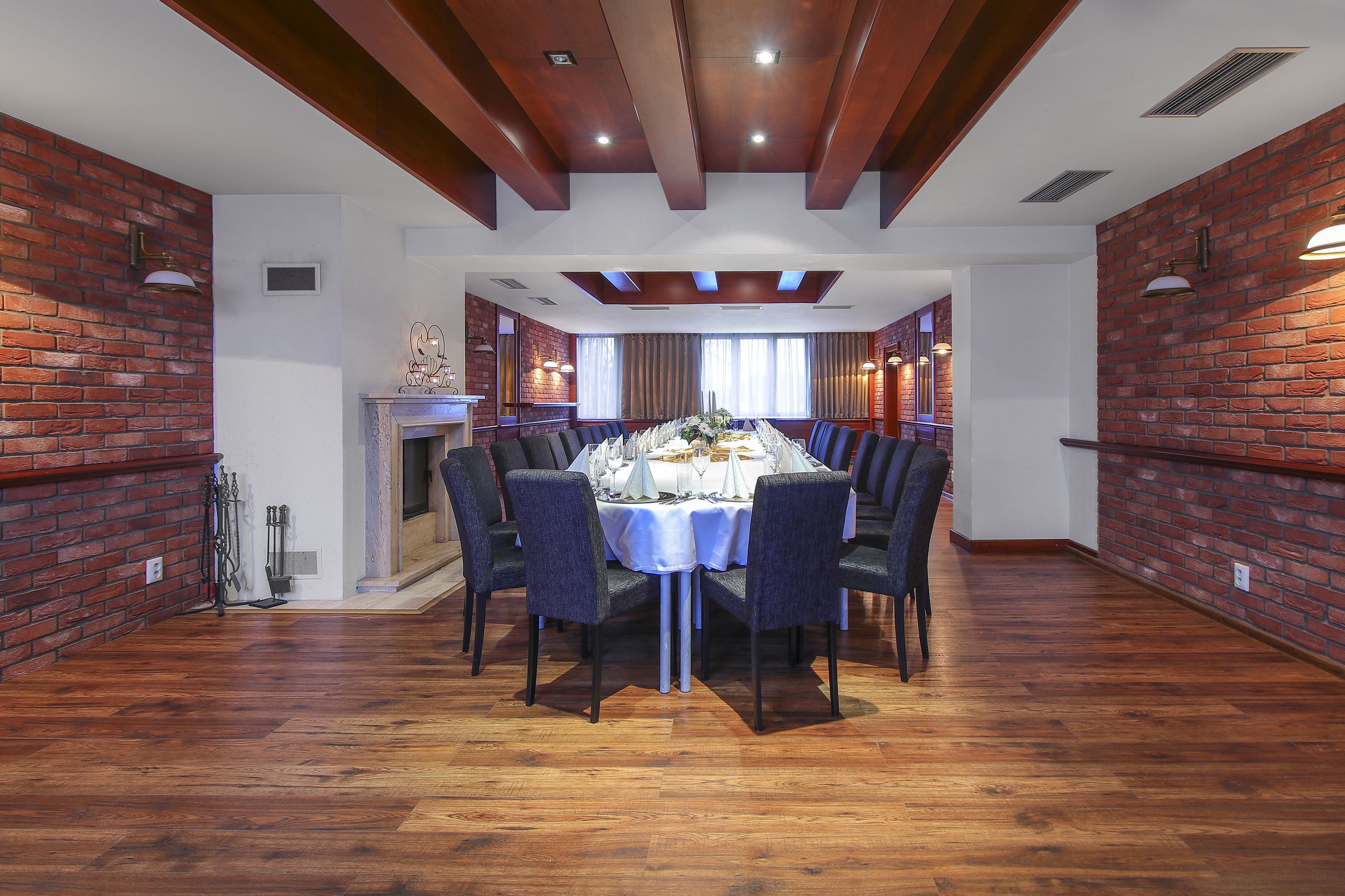 A dining room with a brick wall, wooden ceiling beams, and a round table set for six.