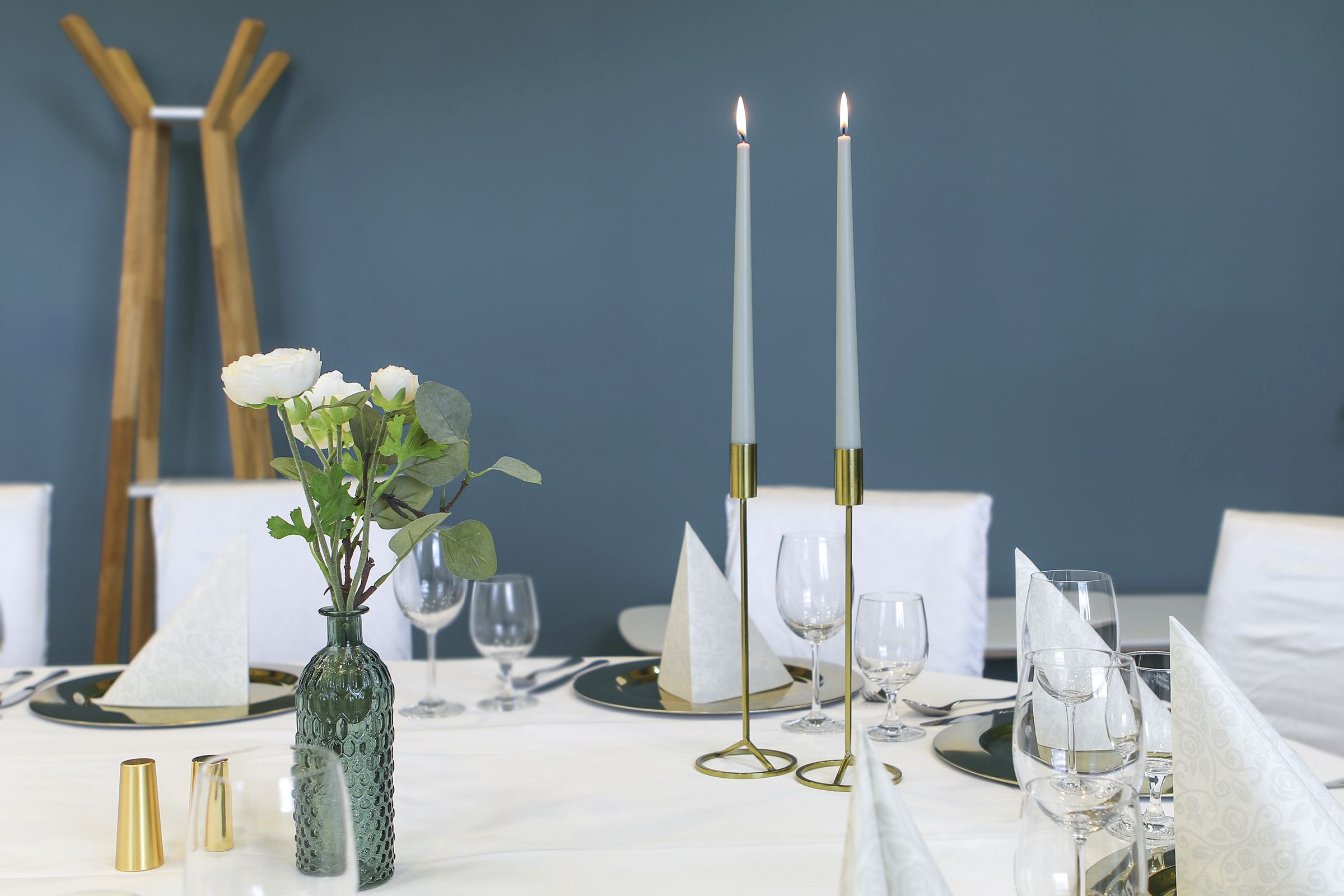 A dining table set with white tablecloth, gold cutlery, and white napkins.