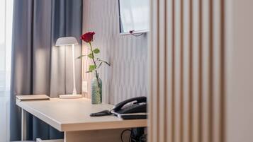 Ett hotellrum med ett skrivbord i trä, en lampa, en vas med en ros och en telefon.