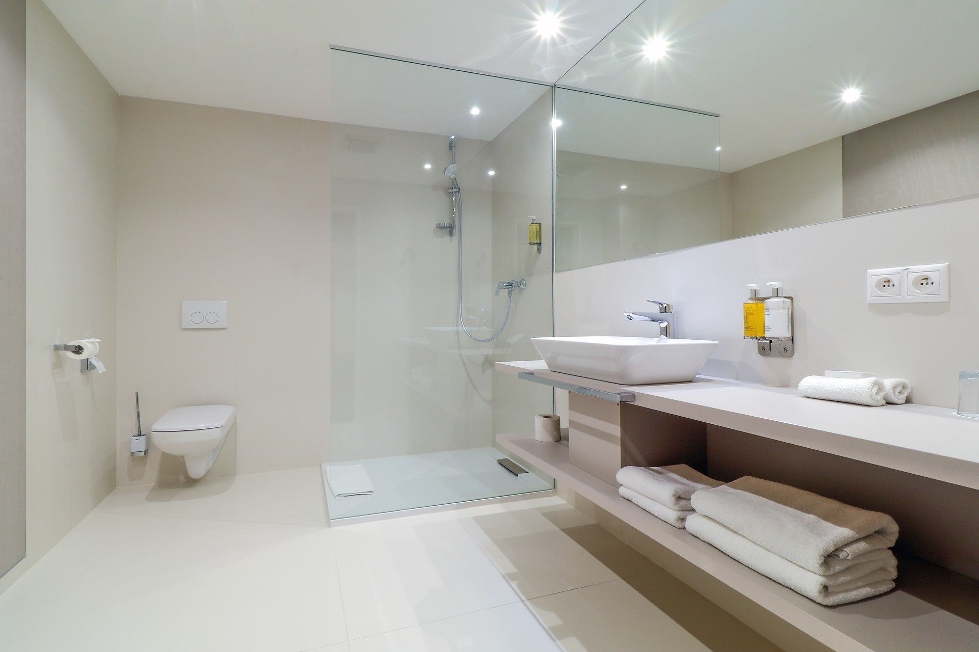 Un baño moderno con ducha de vidrio, un lavamanos blanco y un espejo sobre el mueble.