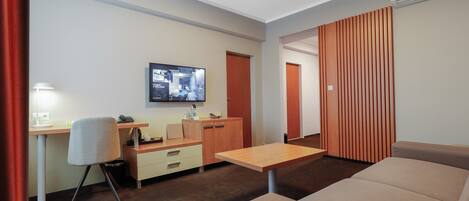 Una habitación de hotel moderna con sofá, escritorio, silla, televisor y un separador de madera.