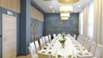 A long dining table set for a formal event, with white chairs and gold accents, in a room with blue walls and a mural.