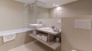 A modern bathroom with a white sink, mirror, and towel rack. There is a shelf with towels and toiletries.