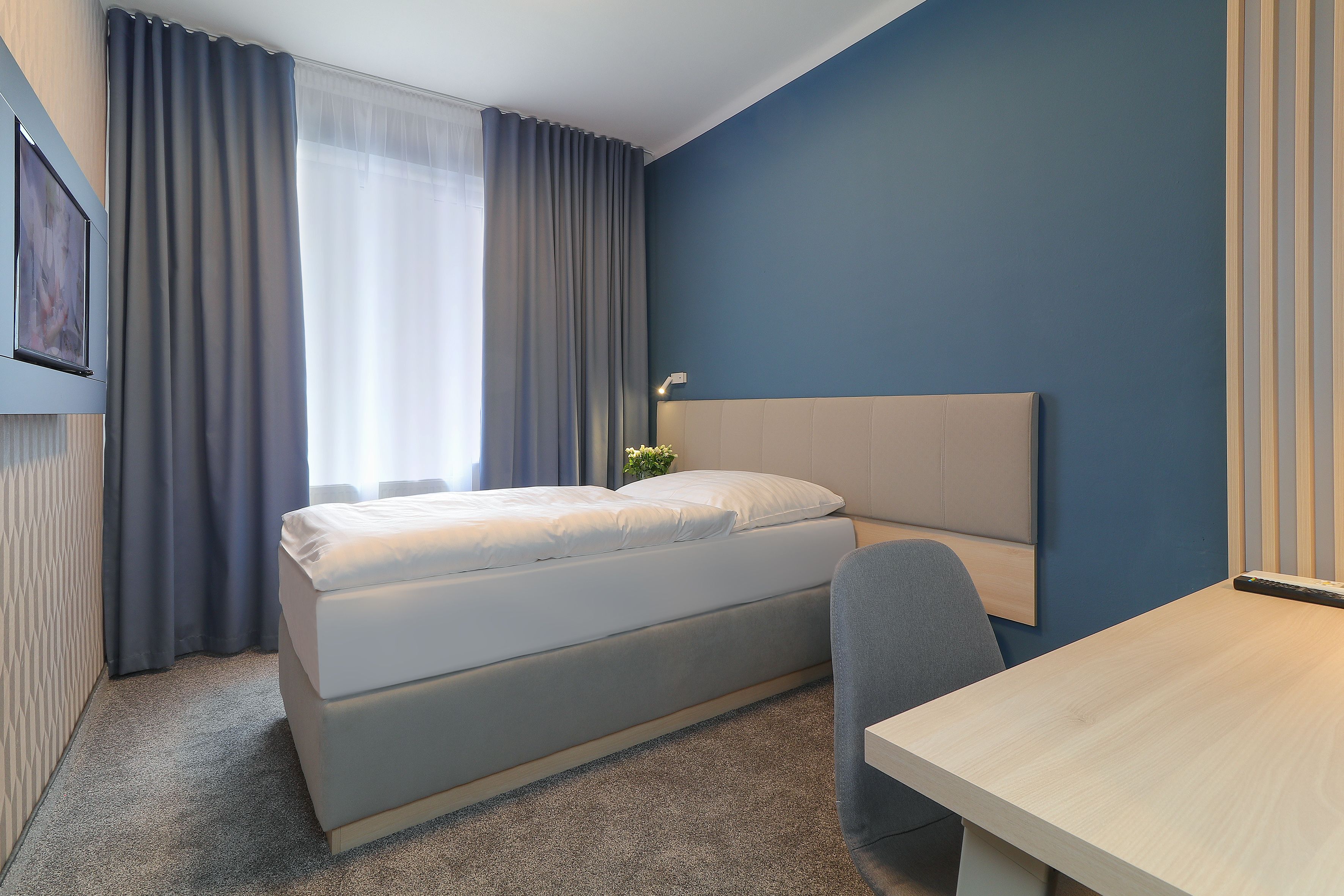A modern hotel room with a bed, a desk, and a chair.
