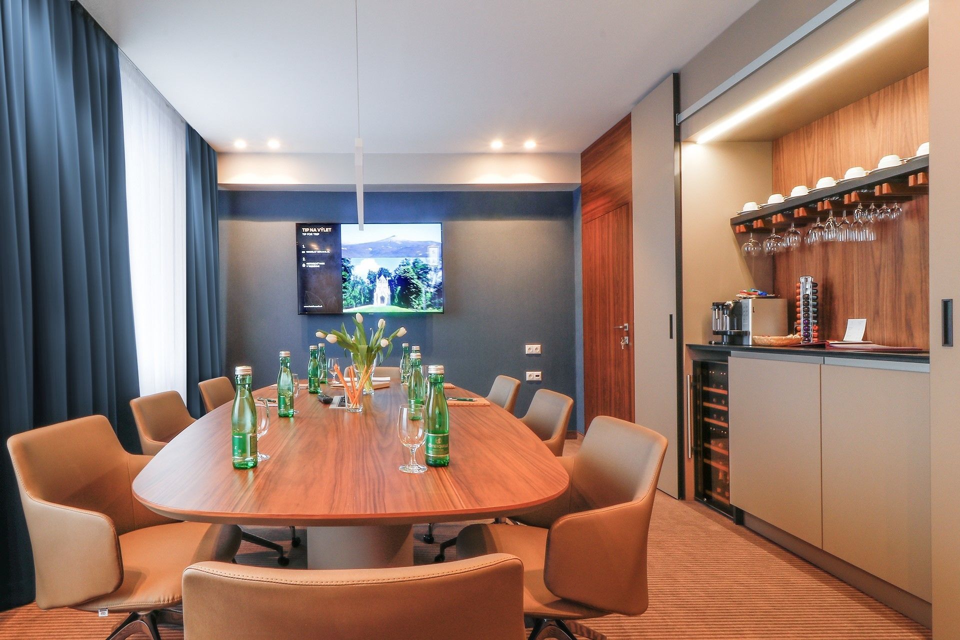 A conference room with a wooden table, leather chairs, and a TV screen on the wall.