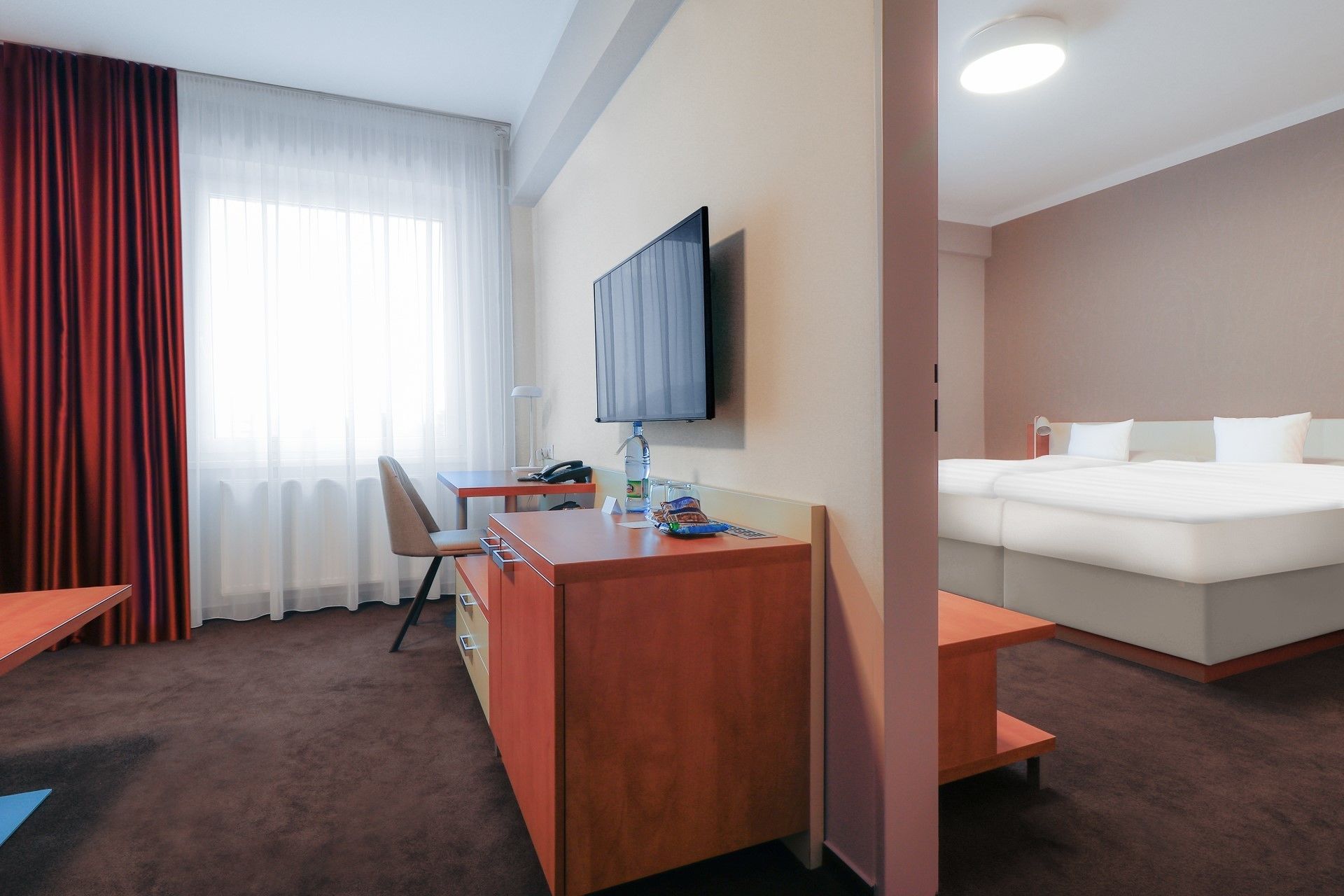 A hotel room with a bed, a desk, a chair, a TV, and a window with curtains.