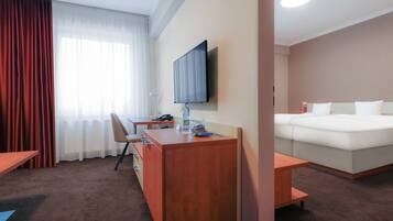 A hotel room with a bed, a desk, a chair, a TV, and a window with curtains.