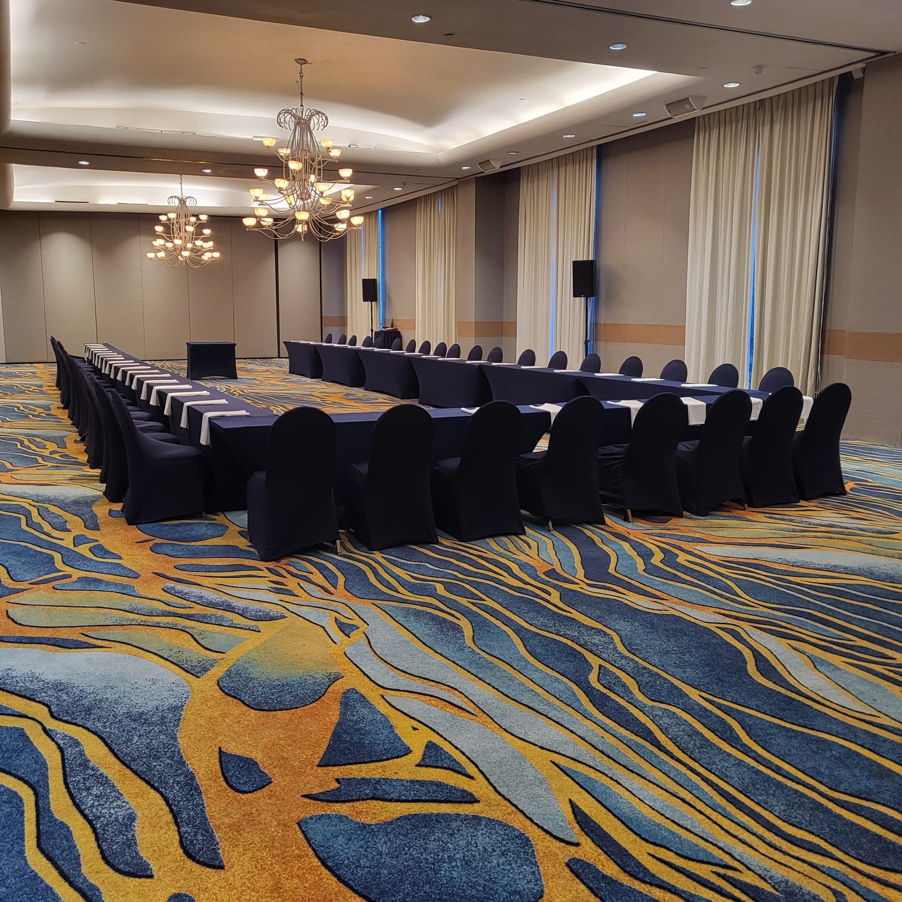 A conference room with a long table, black chairs, a chandelier, and a patterned carpet.