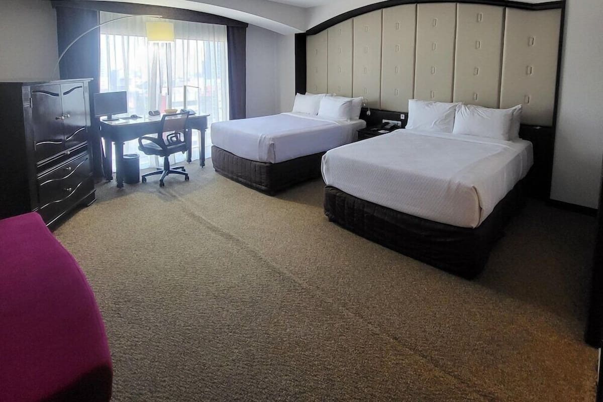 Habitación de hotel con dos camas, un escritorio y una televisión.