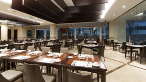 Un vaste espace dédié à la salle à manger, avec de nombreuses tables et chaises, de grandes fenêtres et un design moderne au niveau du plafond.