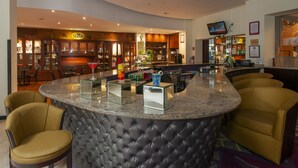 Un bar moderne doté d’un comptoir incurvé en granit, de tabourets confortables et d’une variété d’ustensiles et de bouteilles.