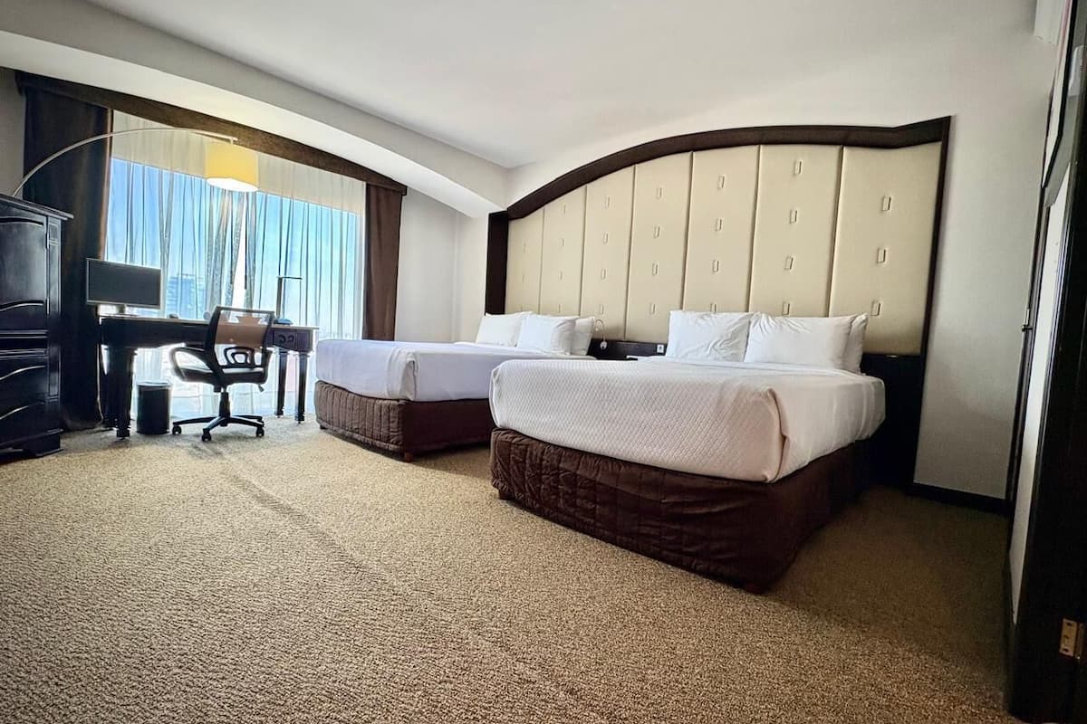 Habitación de hotel con dos camas, un escritorio, una silla y un ventanal grande.