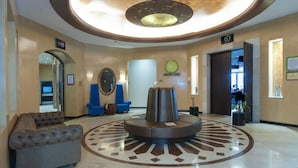 Un hall d’entrée avec un espace salon central, un canapé capitonné, une table ronde et un miroir fixé au mur.