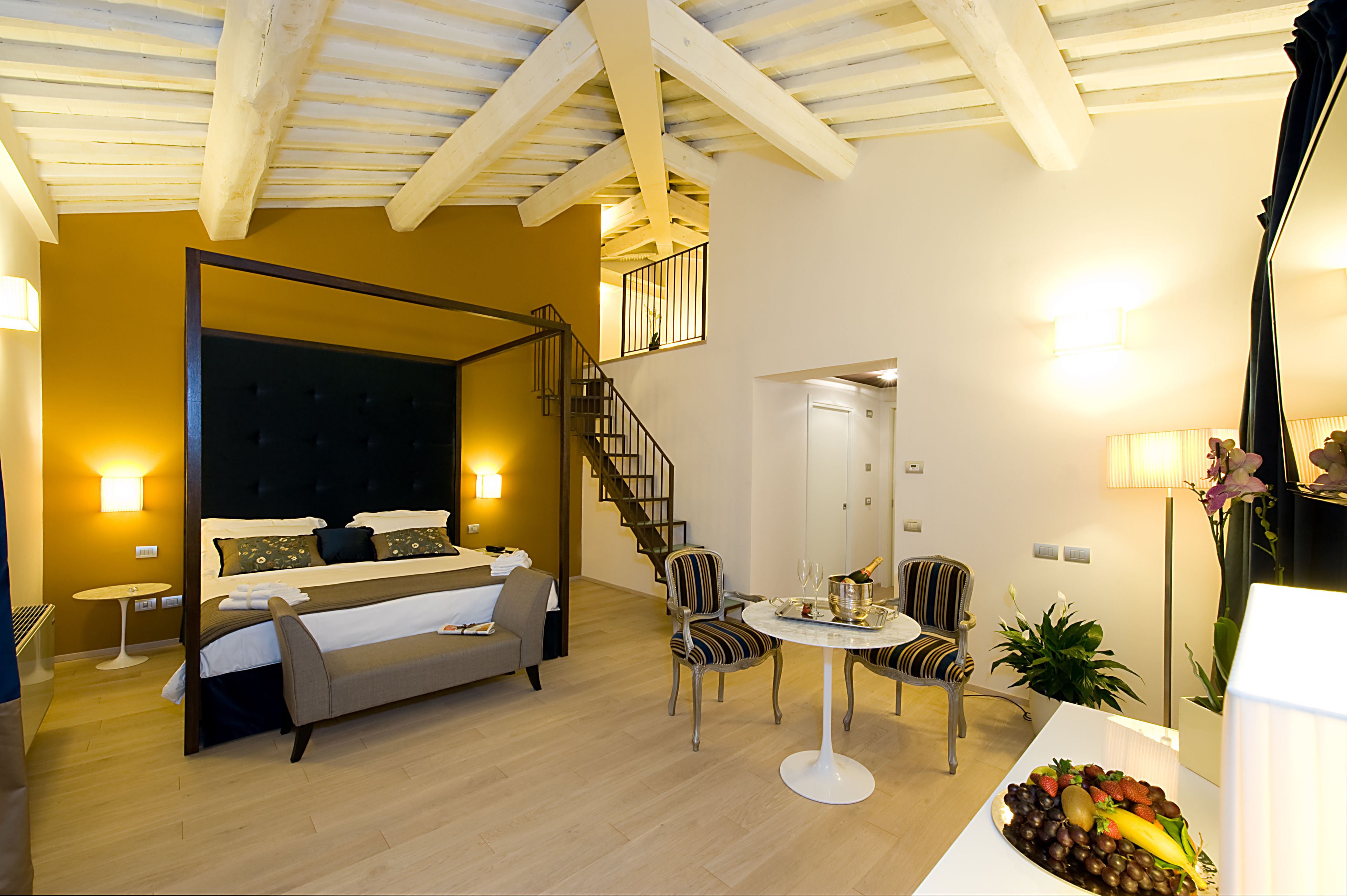 Une chambre à coucher avec un lit à baldaquin, un coin salon avec une table et des chaises, et un escalier menant à un niveau supérieur.