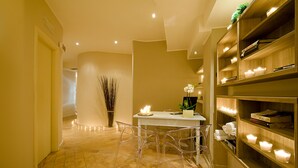 A hallway with a white table and chairs, a vase with white flowers, and shelves with candles and books. - Relais dell'Olmo (Perugia)