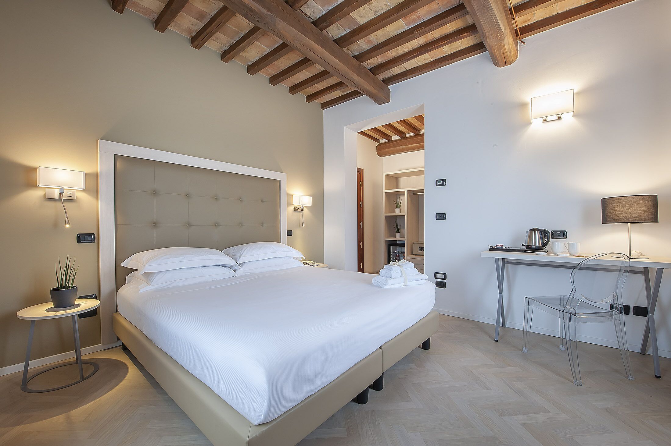 A bedroom with a large bed, bedside tables with lamps, a desk with a chair, and a wooden ceiling.