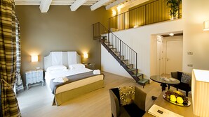 A bedroom with a bed, bedside tables, a nightstand, a desk, a chair, a dining table with a fruit plate, a staircase, and a door. - Relais dell'Olmo (Perugia)