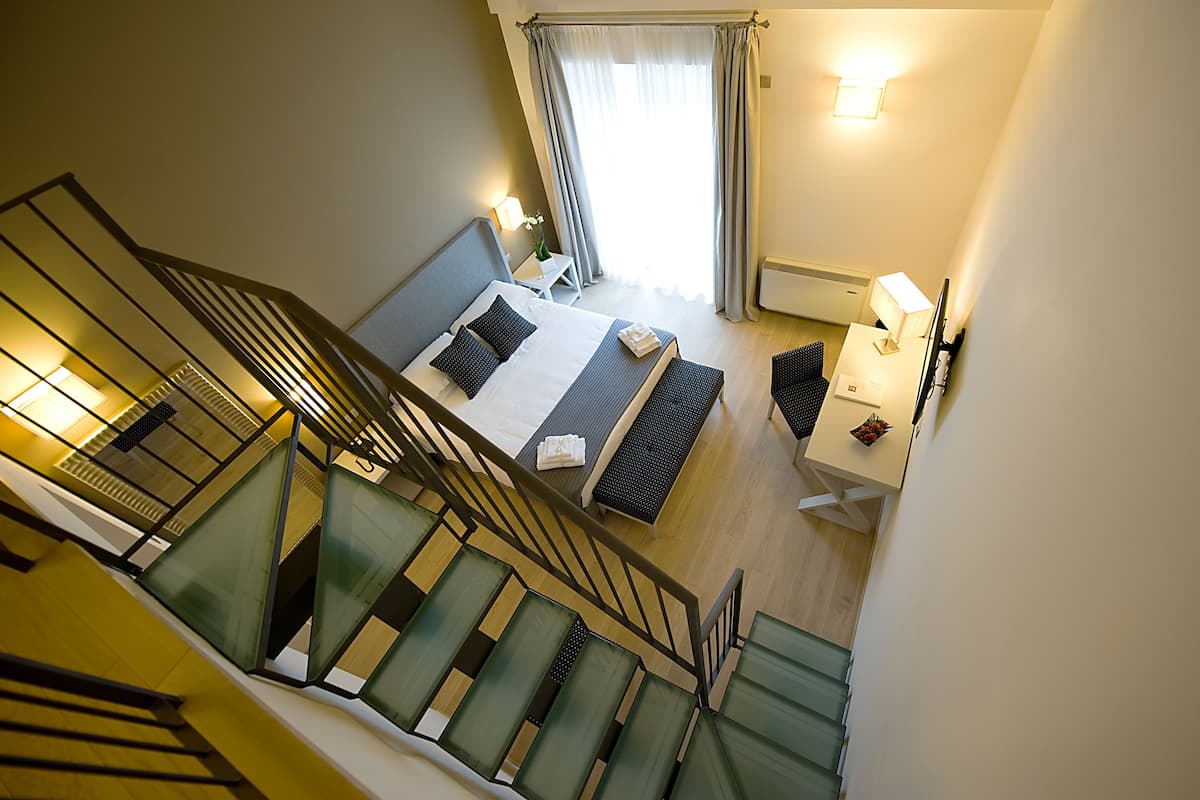 Una habitación de hotel con cama, escritorio, silla, lámpara y una escalera.