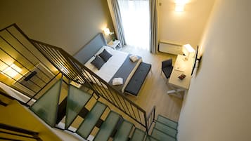 Una habitación de hotel con cama, escritorio, silla, lámpara y una escalera.