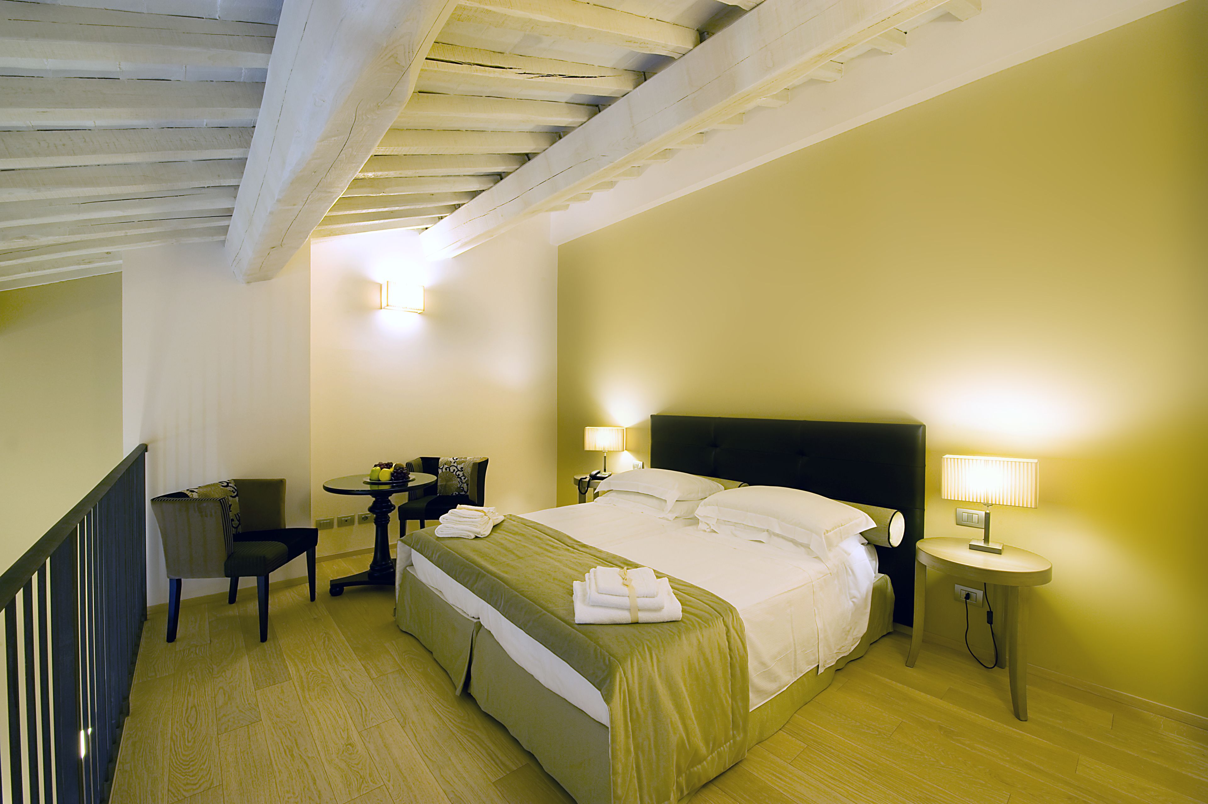 Quarto de hotel com cama, mesas de cabeceira, uma cadeira e escrivaninha.