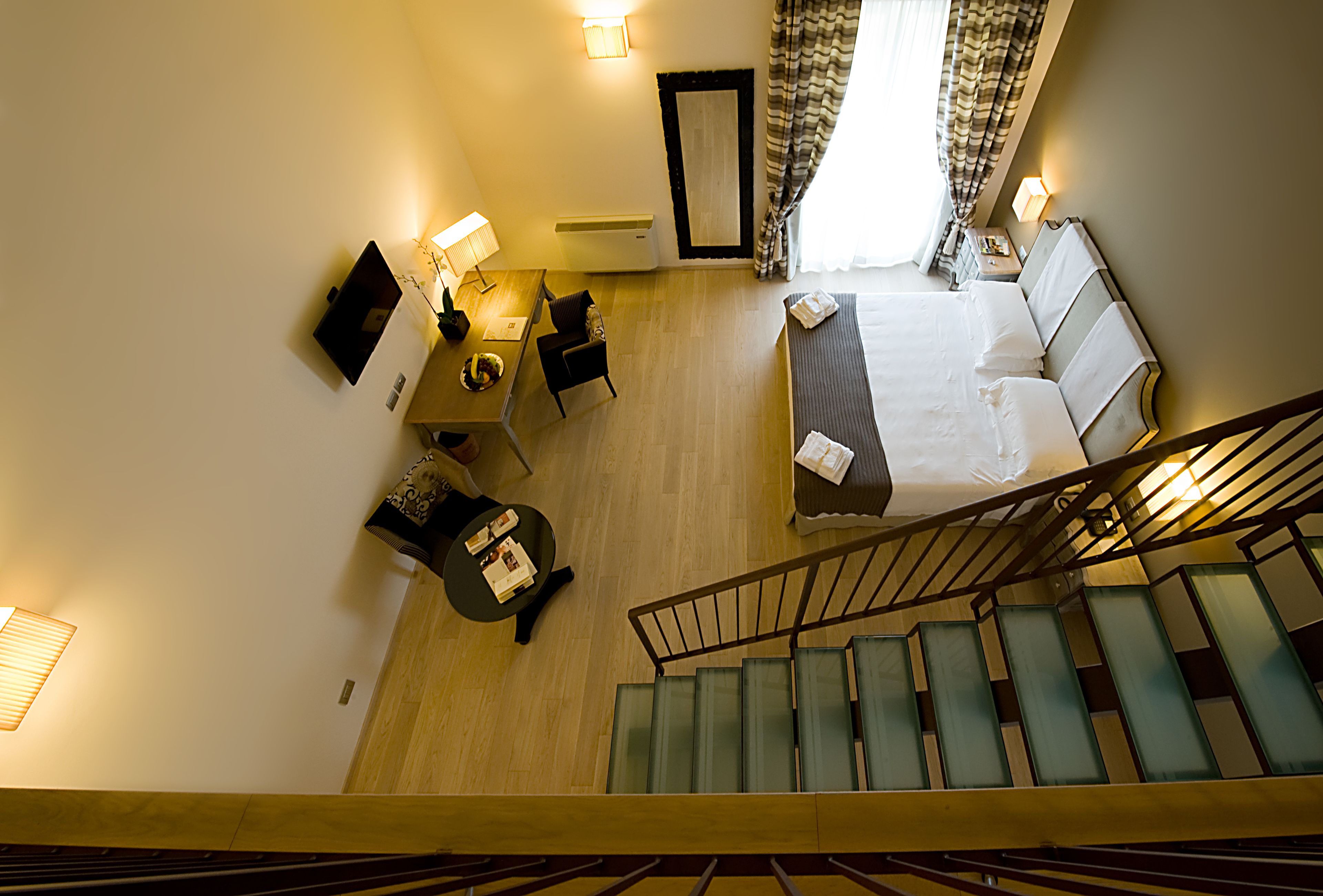 Hotellihuone, jossa on sänky, työpöytä, tuoli, pieni pöytä, lamppu, peili ja portaat.
