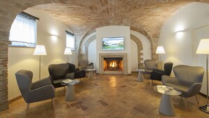 A room with a fireplace, leather chairs, and a television mounted on the wall. - Relais dell'Olmo (Perugia)