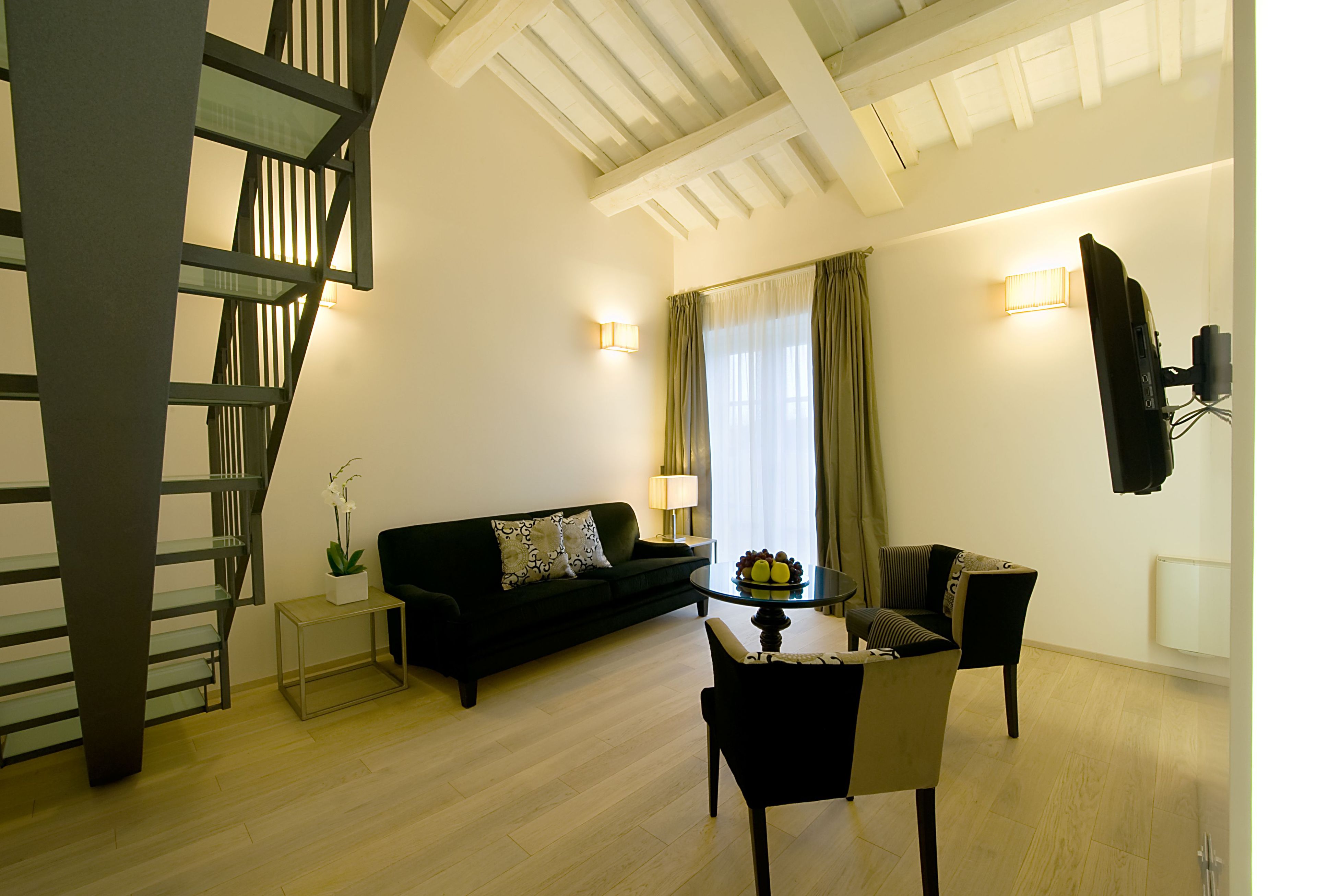 Un salon moderne avec un escalier, un canapé noir, une table à manger avec des chaises et une lampe.