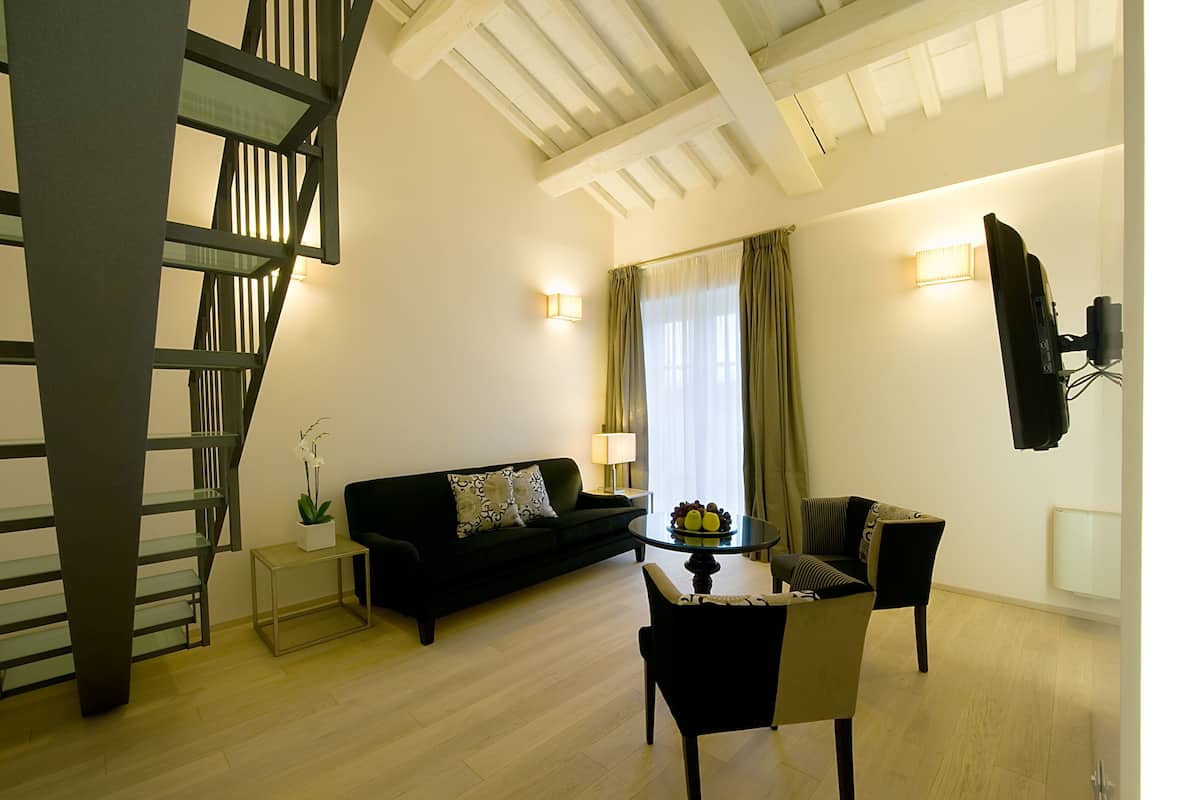 Una sala de estar moderna con una escalera, un sofá negro, una mesa de comedor con sillas y una lámpara.