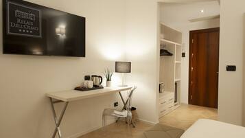 A hotel room with a desk, chair, TV, and closet.