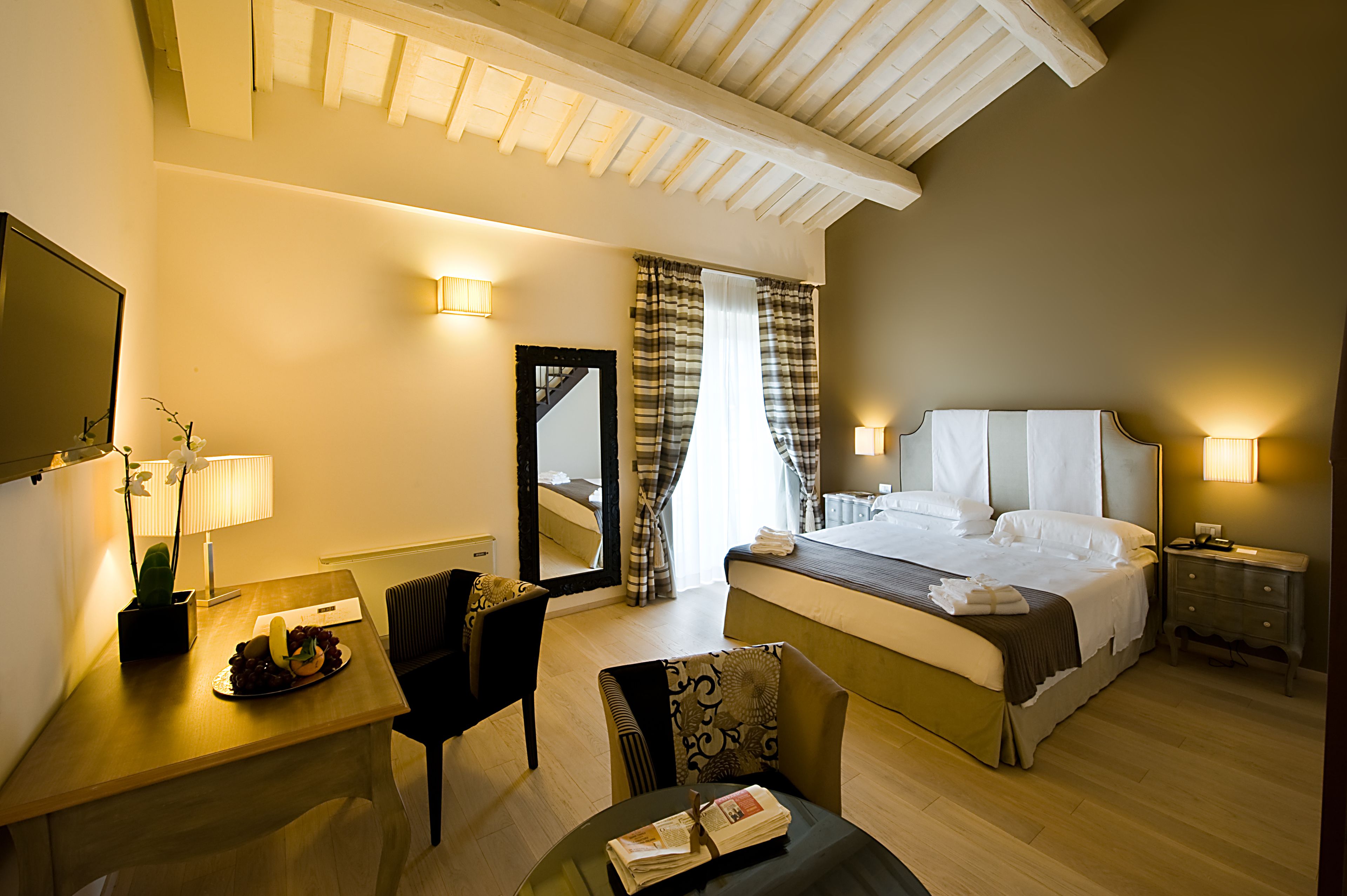 Habitación de hotel con cama, mesita de noche, lámpara, silla y escritorio con planta y fruta.