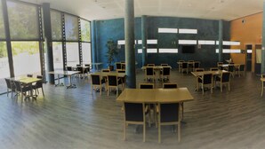 A spacious room with multiple tables and chairs, large windows, and a plant. - Holiday Inn Express Barcelona - Molins de Rei by IHG (Molins de Rei)