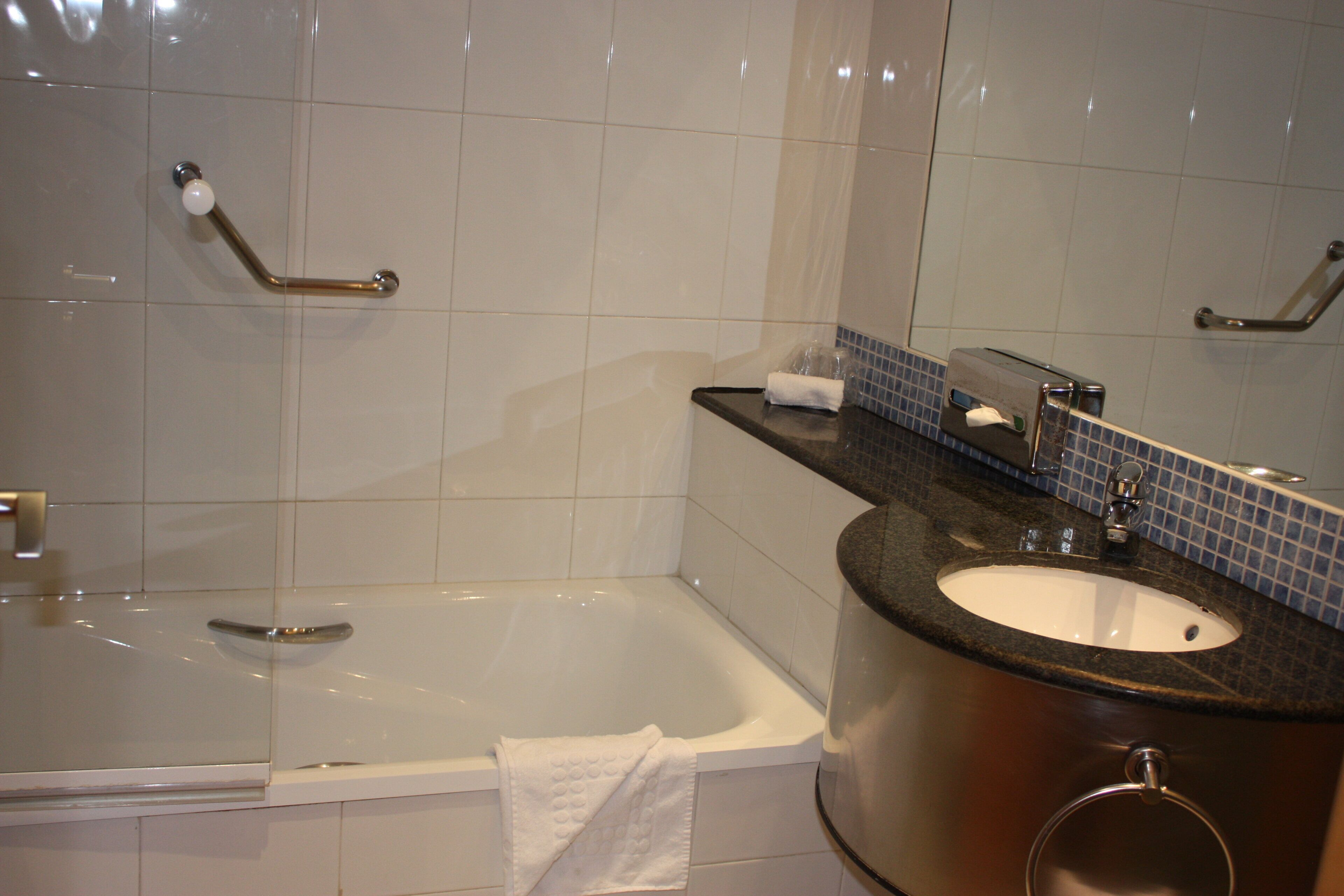 Une salle de bain équipée d’une baignoire, d’un lavabo, d’un miroir et de barres d’appui.