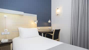 A hotel room with a bed, desk, chair, and a phone on the nightstand.