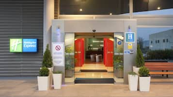 De buitenkant van een Holiday Inn Express hotel met een duidelijke ingang, een rookvrij bord en een herkenbaar ‘H’ logo dat een hotel aanduidt.
