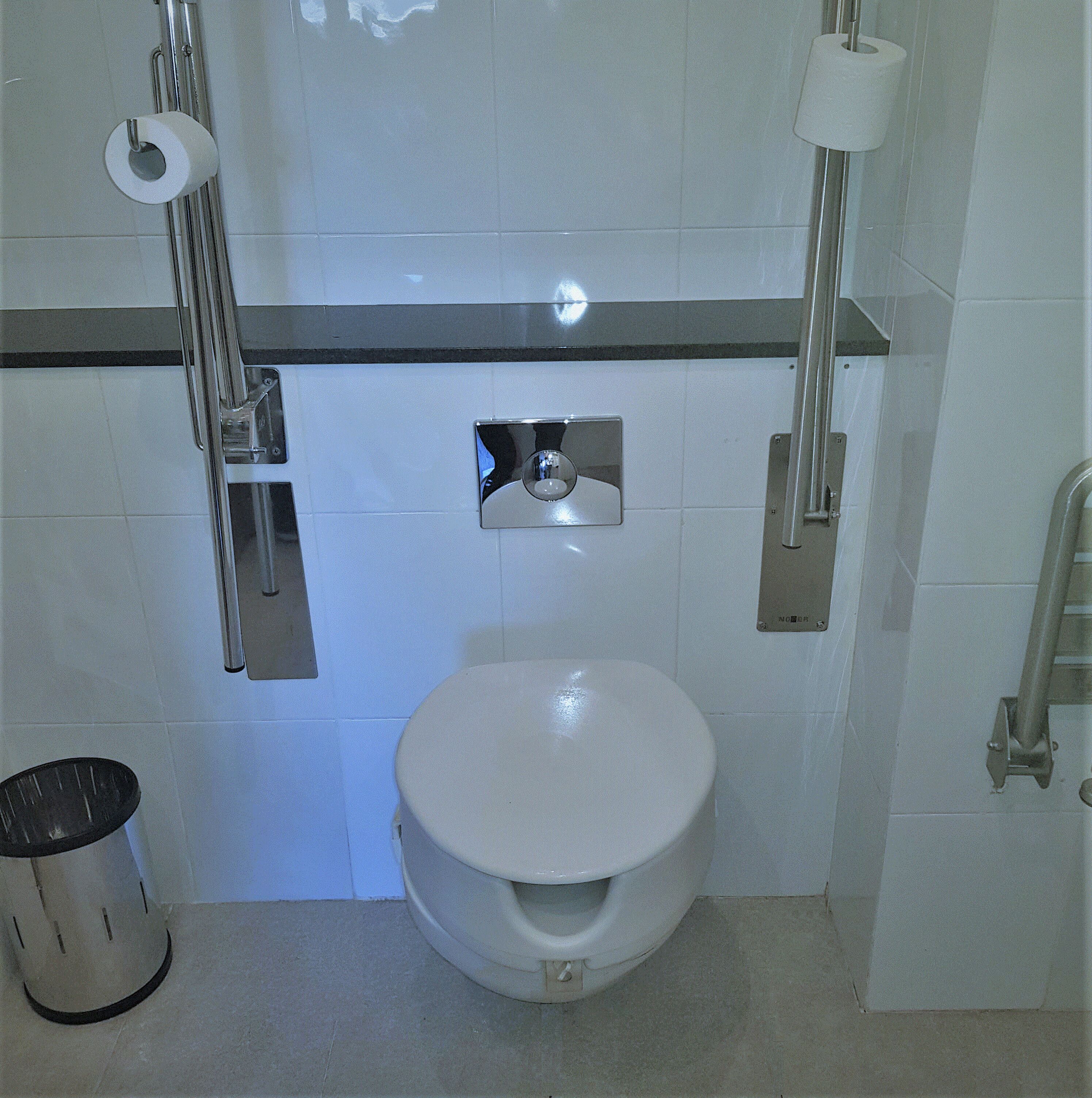 A standard bathroom with a toilet, a hand dryer, and a trash can.
