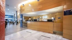 A modern hotel reception area with a wooden reception desk, a digital clock, and a seating area with tables and chairs. - Holiday Inn Express Barcelona - Molins de Rei by IHG (Molins de Rei)