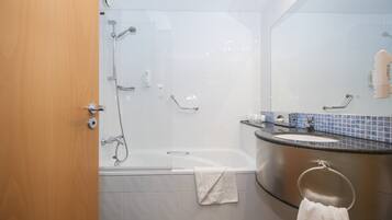 Un baño moderno con ducha de vidrio, bañera independiente y lavamanos curvo con argolla para toallas.