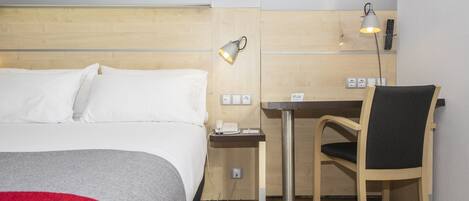 A hotel room with a bed, a desk, a chair, and a lamp.